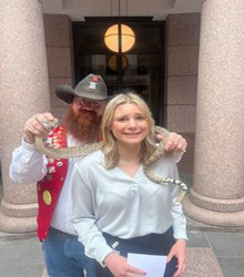 Abby Powell stands in fear next to a man holding a snake over her shoulder.